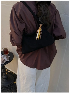 Detail view of black suede shoulder bag with colorful wooden bead pendant outdoors