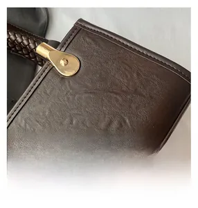 Detail of dark brown lychee leather handbag featuring a woven handle and gold hardware