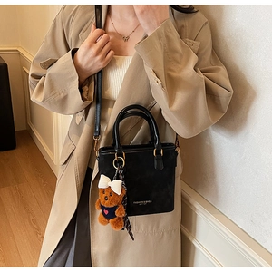 Detail of black matte handbag with gold text and a cute brown plush bear charm