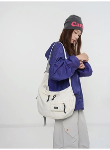 Détail d'un sac bandoulière en toile blanche avec tirette tissée et étiquette carrée frontale