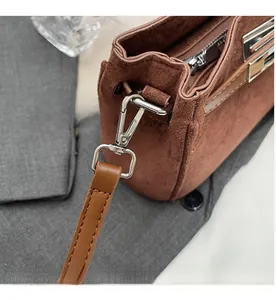 Detail of silver hardware clasp and strap on brown suede leather crossbody bag