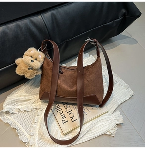 Detail of dark brown suede hobo bag with plush bear charm on white fabric and art book