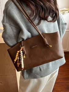 Retro brown leather tote bag with wooden bead charm shown in a minimalist shoulder carry style