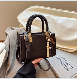 Detail of dark brown vintage handbag with woven handle and wooden bead tassel accessory