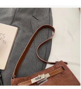 Close-up of brown suede Kelly bag with silver metal clasp and leather strap detail