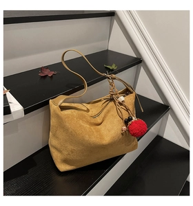 Nahaufnahme der khakifarbenen Wildledertasche mit Ethno-Anhänger auf Holztreppen