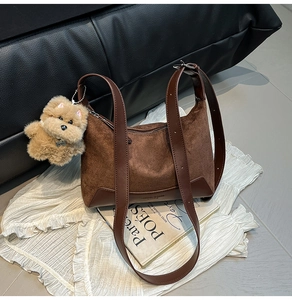 Detail of brown suede shoulder bag with long leather strap and plush dog charm
