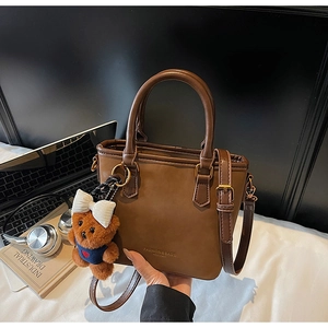 Detailed close-up of brown matte leather bucket bag with white bear charm and gold text