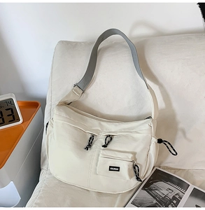 Détail d'un sac bandoulière en toile crème avec large bandoulière grise sur un canapé