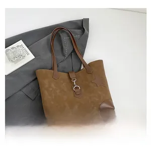 Detail der braunen Wildledertasche mit Stern-Patch und Metallschließe auf grauem Sakko