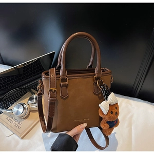 Detail view of brown suede tote bag with teddy charm, laptop, and books on desk