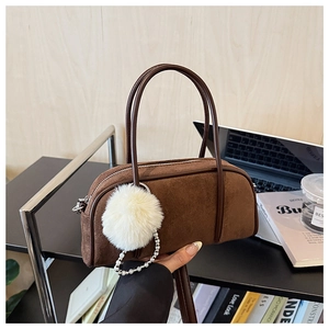 Detail of a brown suede bowling bag with fluffy pompom and pearl chain on a desk