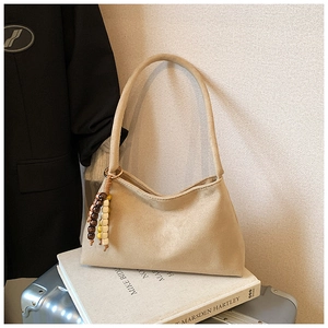 Detail of beige suede shoulder bag featuring a unique wooden bead pendant decoration