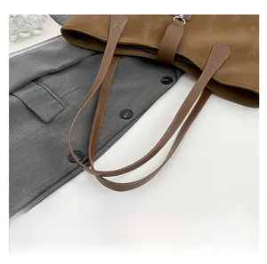 Detail einer braunen Tragetasche mit matter Textur und Schnallenriemen auf grauem Blazer