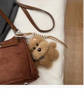 Detail of cute brown plush dog charm with TOP DOG tag hanging on a stylish suede handbag