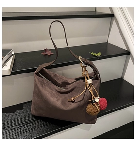 Detail of coffee suede tote bag with fur ball charm and vintage strap on wooden steps