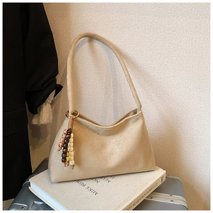 Detail of beige suede hobo bag with bohemian colorful beaded pendant on top of books