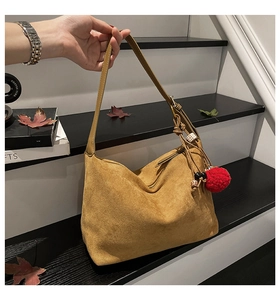 Detail of yellow suede hobo bag with ethnic wooden beads and red pompom tassel