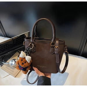 Detail of dark brown matte leather bucket bag with cute bear charm and fashion lettering