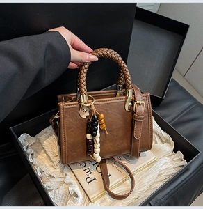 Detail of vintage brown leather bag featuring woven top handle and wooden bead charm
