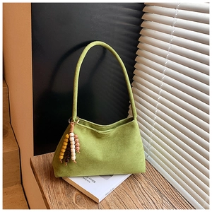 Detail of green suede shoulder bag with bohemian colorful beaded tassel on a book