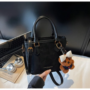 Detail view of black matte bucket bag with golden hardware and plush bear charm