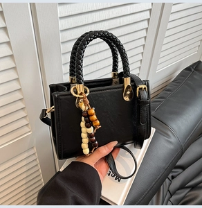 Detail of black crossbody bag featuring woven top handles and beaded tassel accessory