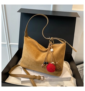 Detail of tan suede shoulder bag with adjustable strap and decorative pompom charm