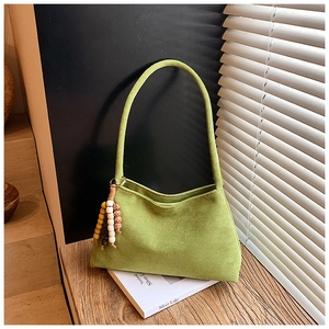 Detail of green suede shoulder bag with bohemian wooden bead tassel in soft sunlight
