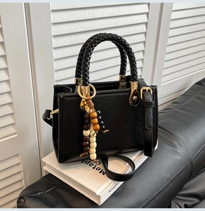 Detail of a vintage black leather handbag with a woven handle and beaded charm accessory