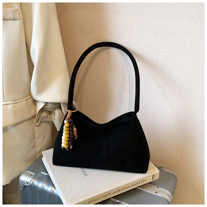 Black suede half-moon shoulder bag with colorful beads on a book and silver suitcase