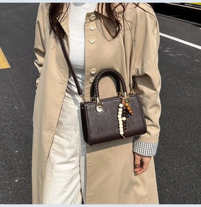 Detailed street view of a vintage dark brown satchel bag with a braided handle and beads