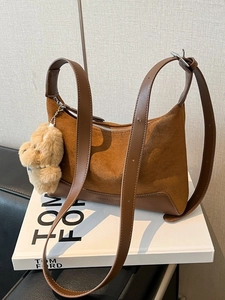 Brown leather hobo bag with teddy pendant on white book against gray wall