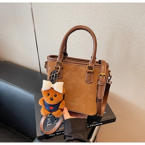 Detail of a brown tote with round handles and a cute teddy bear charm accessory