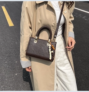 Detail of vintage brown crossbody bag with woven handle and beaded charm on khaki coat