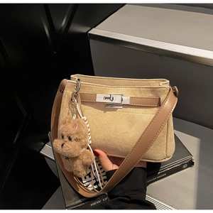 Detail of beige suede crossbody bag with brown leather strap and a plush bear charm