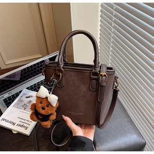 Macro detail of dark brown matte leather tote with fashion logo and bear charm