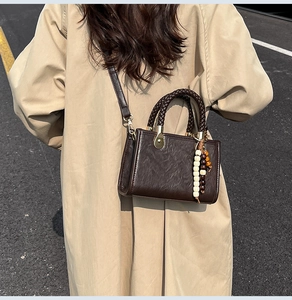 Detail of dark brown leather crossbody bag with braided handle and beaded ornament accessory
