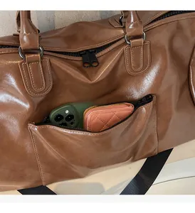 Détail du sac de voyage en similicuir marron montrant une poche zippée pour téléphone et portefeuille