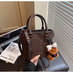 Detail of a dark brown vintage bucket bag with a plush bear charm on a black leather seat