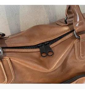 Détail des doubles fermetures éclair noires lisses sur le sac de voyage en cuir marron