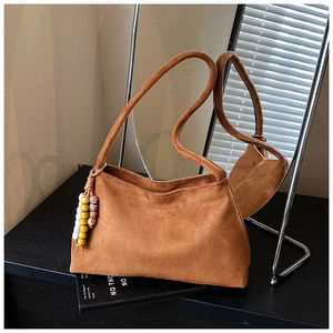 Detail of brown suede shoulder bag featuring bohemian beaded tassel and smooth leather texture