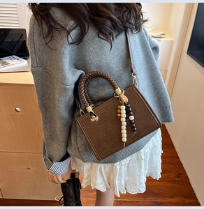 Detail of vintage brown PU leather boston bag with woven handle and beaded pendant charm