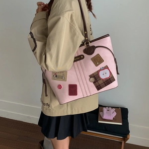 Detail of pink tote bag with cartoon patches and brown straps worn with a casual jacket