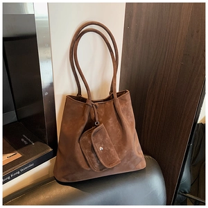 Close-up of brown suede tote bag with a small matching purse on a leather chair