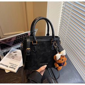 Detail of black suede tote bag with teddy bear charm and adjustable leather strap