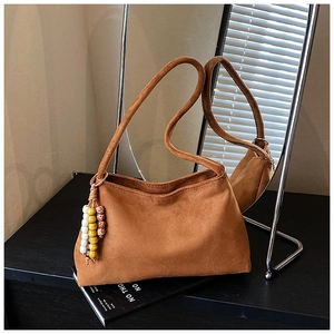 Detail of a brown suede shoulder bag with a colorful beaded pendant and sleek strap