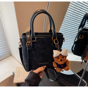 Detail of black crossbody bag featuring suede textures and a cute brown bear charm