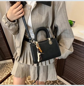 Close-up of black leather crossbody bag with wooden bead charm on a grey blazer outfit