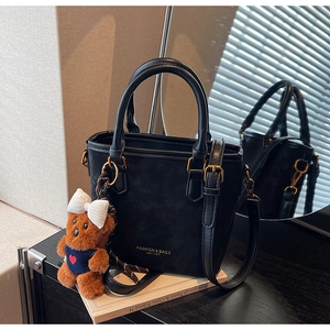 Detail of black suede bucket bag featuring leather handle and brown bear charm accessory